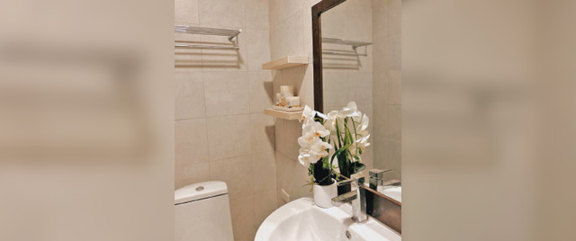 A bathroom featuring a toilet, sink, and mirror, with neutral-colored walls and tiled flooring.